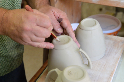 Eine Hand ritzt ein Zeichen in den Boden einer Tasse